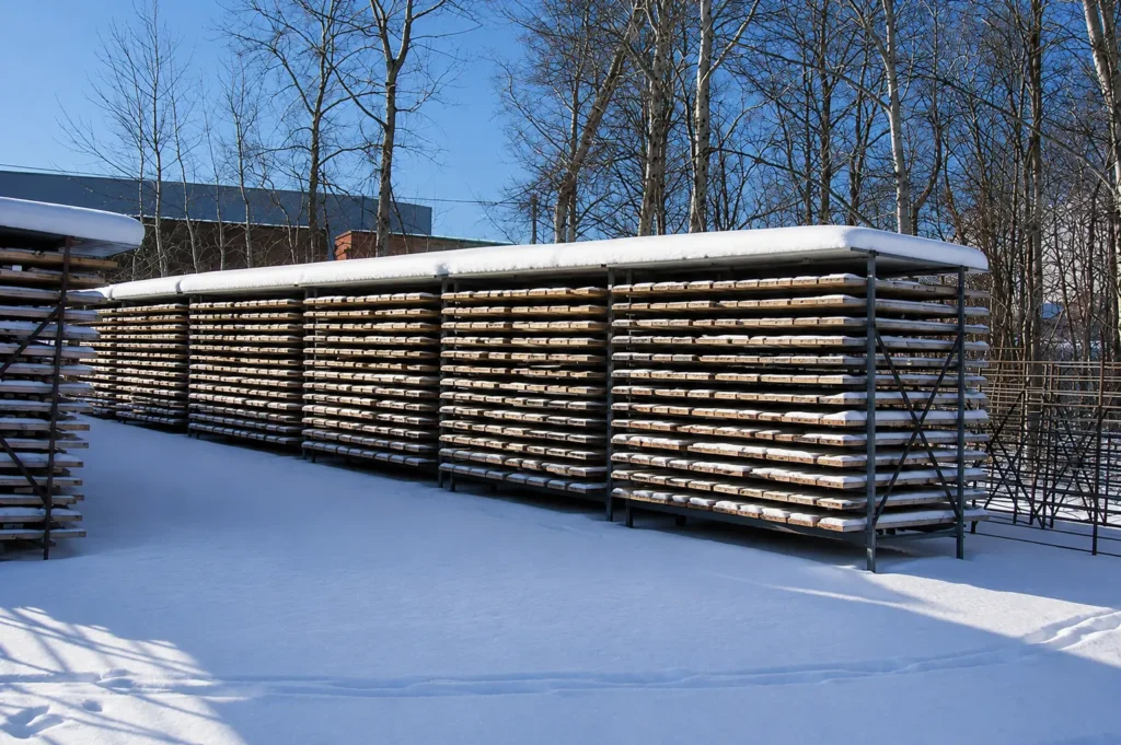 Snow-covered row of stationary Korax core racks with roofed covers, fully loaded with wooden core boxes in a winter exploration yard.