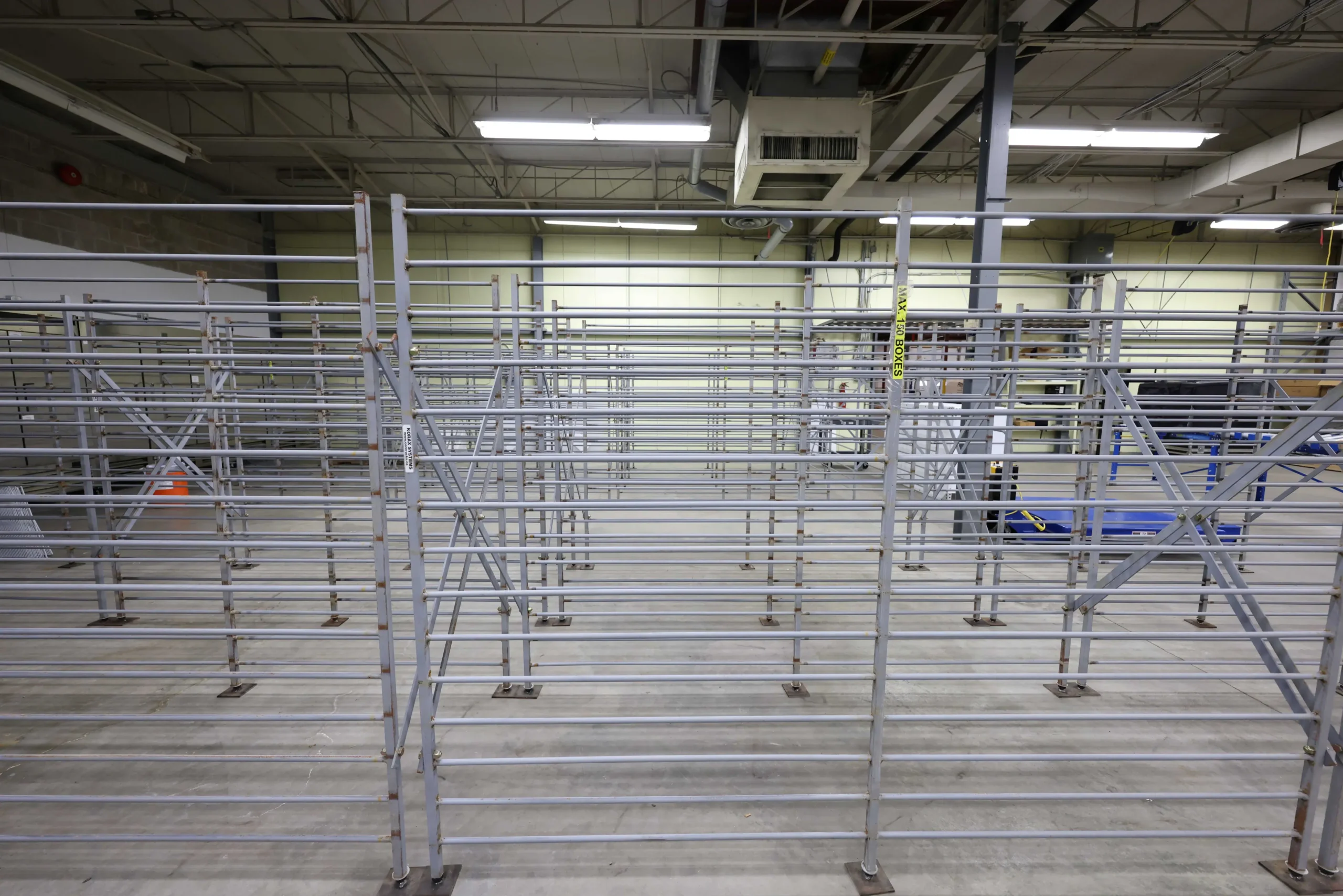 Rows of empty Korax steel core racks in a warehouse, with a visible "Korax Systems" branded tag and maximum capacity label on the nearest rack.